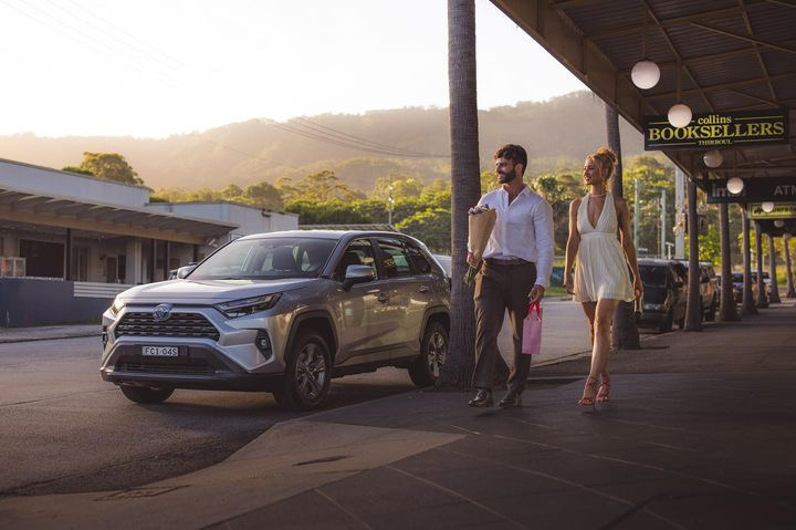 Toyota RAV4 parked on a coastal main street at golden hour, Shanti Griffin walking past